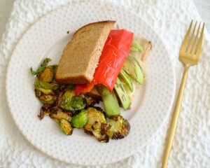 roasted pepper sandwich with sliced avocado and roasted brussels sprouts