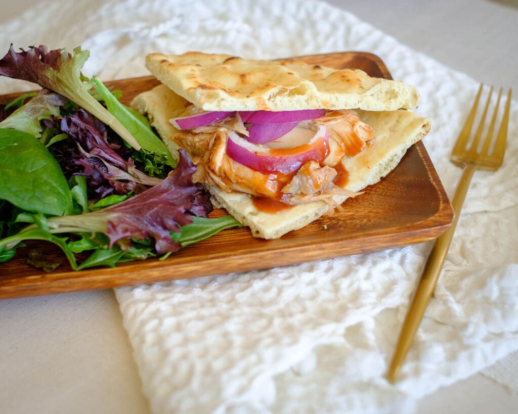 rectangular wooden plate with chicken flatbread and spring mix salad